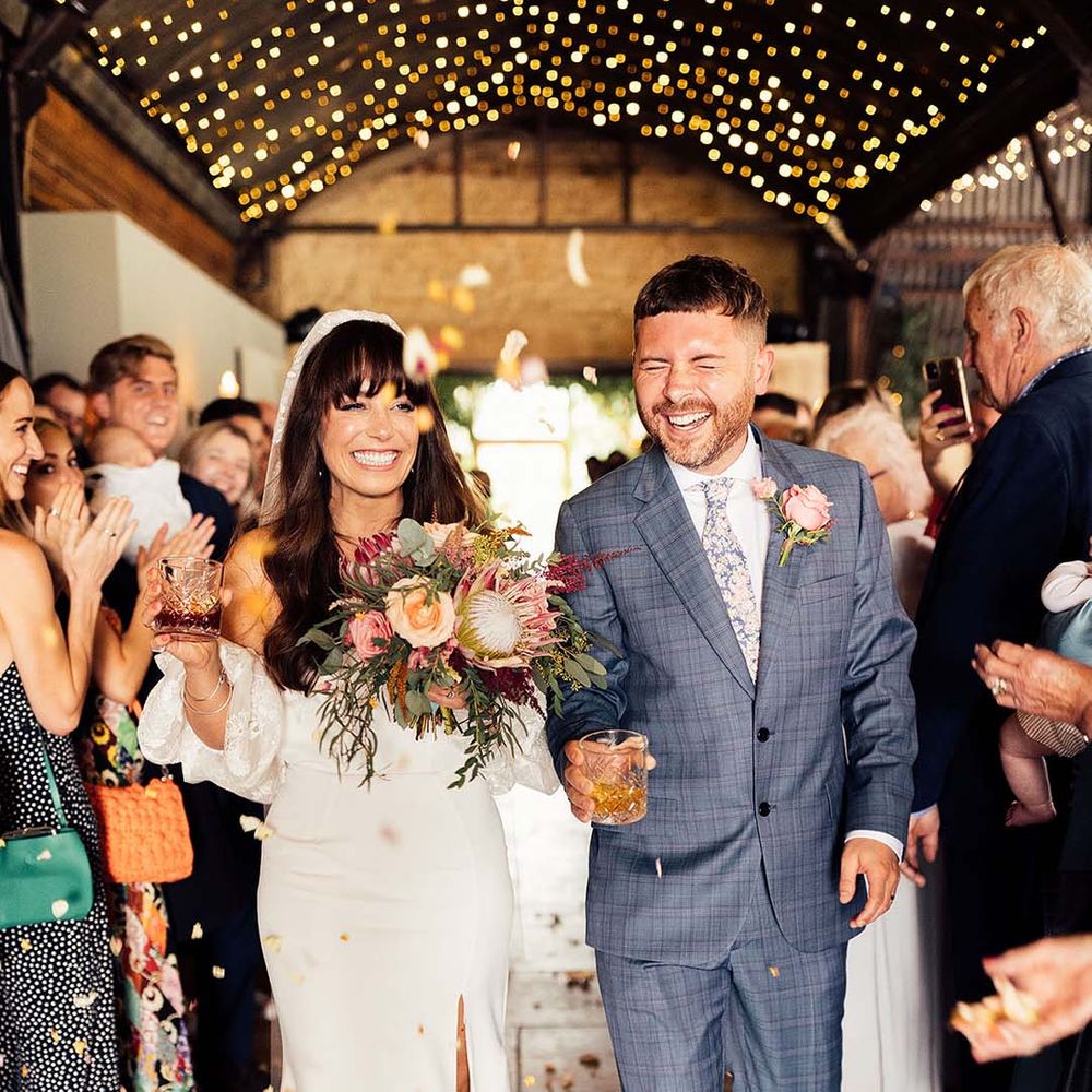 Bride & groom walk down the aisle as wedding guests throw confetti around them 