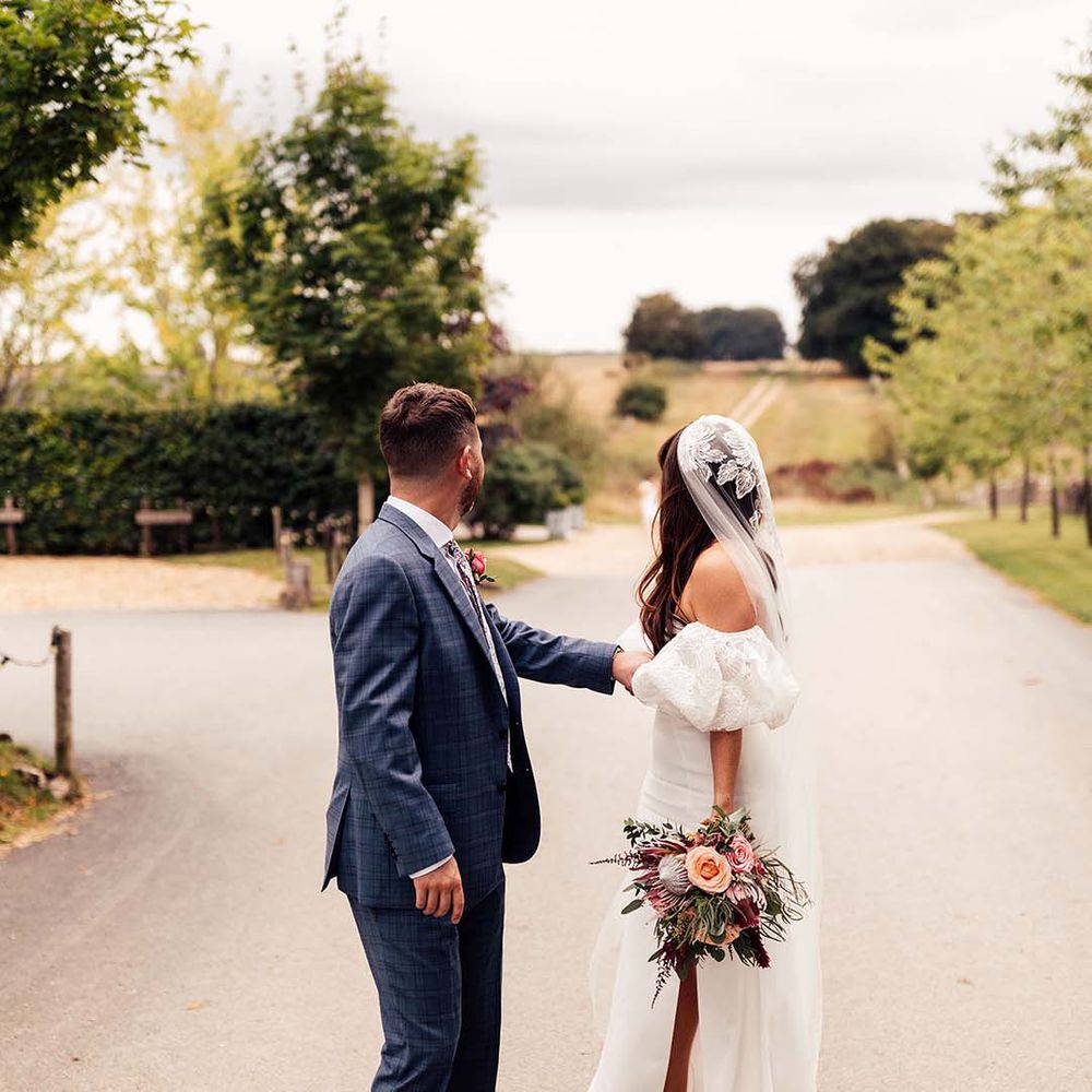 Groom in a blue check suit and bride in a strapless wedding dress with lace detachable sleeve and veil at their Stone Barn Cotswolds wedding 