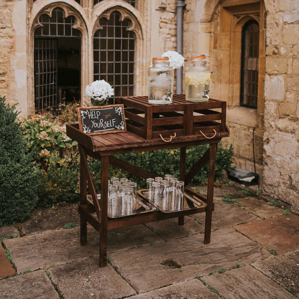 Wooden table and crates with drinks dispensers and glasses for outdoor wedding ceremony