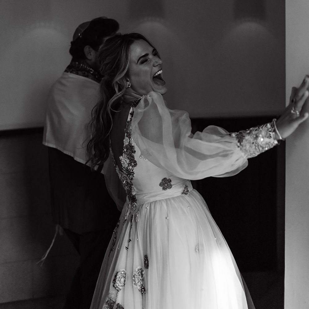 Bride in mesh sleeve embroidered wedding dress laughs as her and groom leave wedding ceremony
