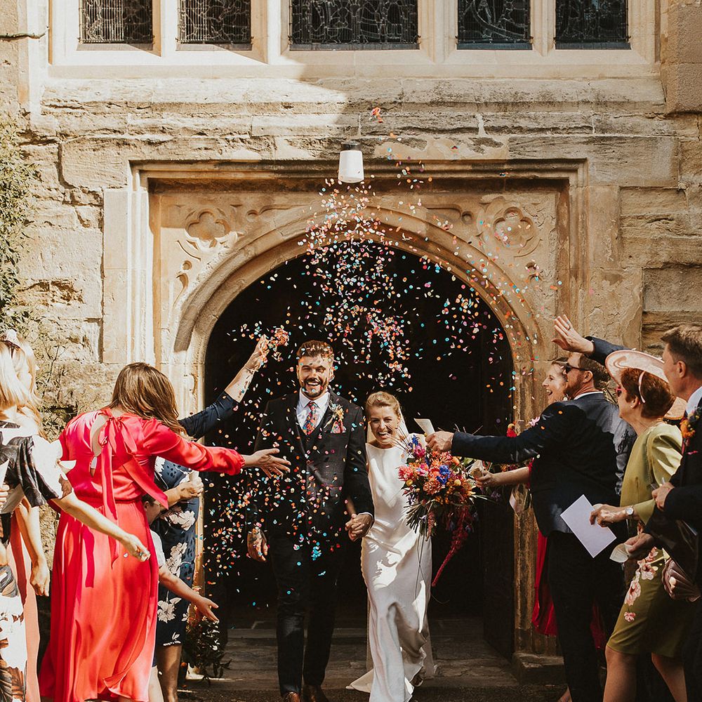 Colourful couch confetti exit with groom in a navy three piece suit and bride in a Charlie Brear wedding dress