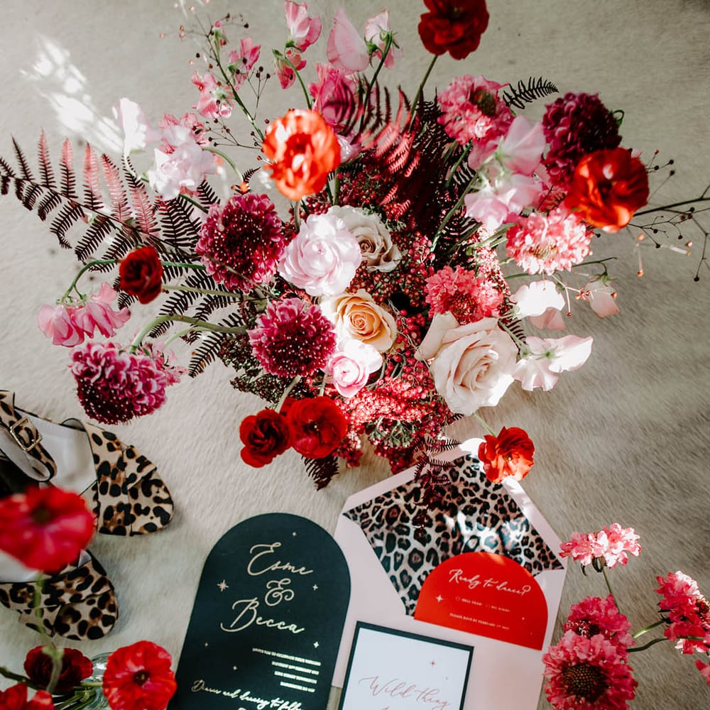pink and red flowers and flatlay of wedding stationery suite with leopard print lined envelopes and goild foil lettering and tassel detail 