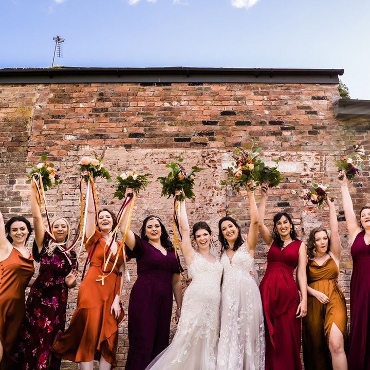 Purple, yellow, orange and red jewel tone bridesmaids dresses for autumnal theme lesbian wedding at Foxtail Barns wedding venue