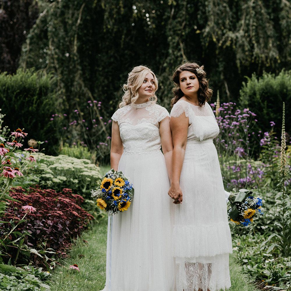 Brides holding colourful bouquets stand together in pretty gardens at Chaucer Barn 