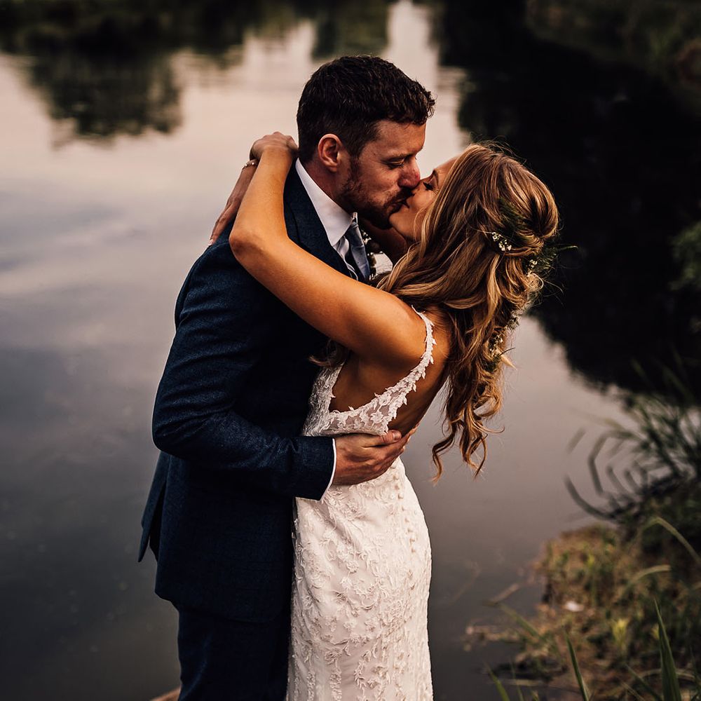 Bride and groom kiss in front of lake 