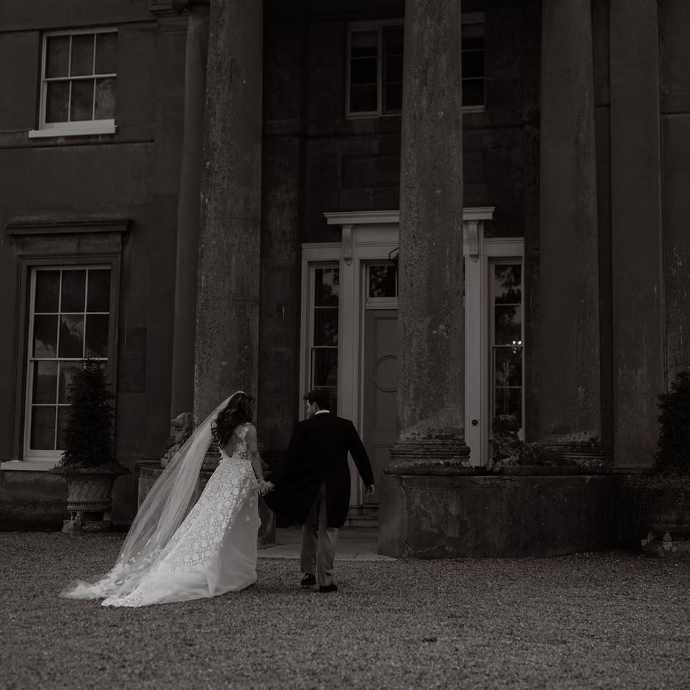Bride in flower applique wedding dress with groom in morning suit outside their wedding venue 