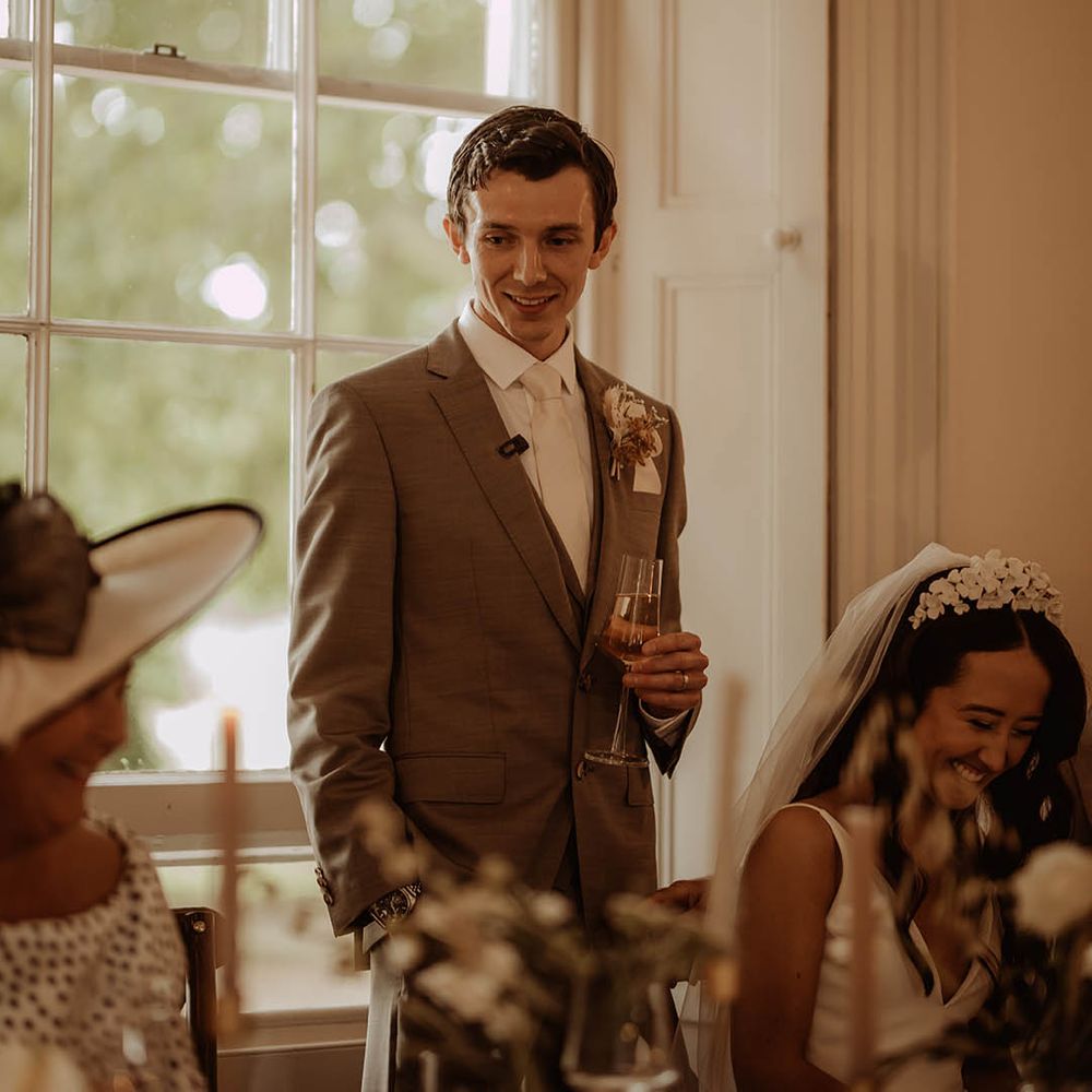 Groom stands up as he gives a speech in a neutral three piece suit with a dried buttonhole 