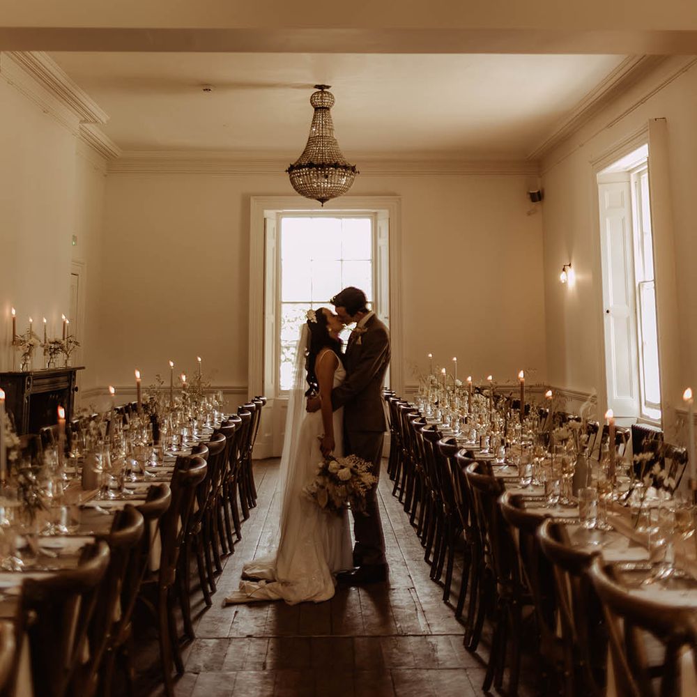 Bride and groom share a kiss in their wedding reception room with banquet tables and dried flower minimal decor 