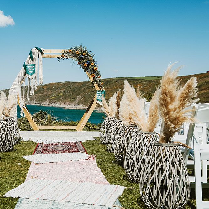 Wicker vases holds pampas grass bouquets lining aisle with Moroccan styled rugs and DIY wooden arch 