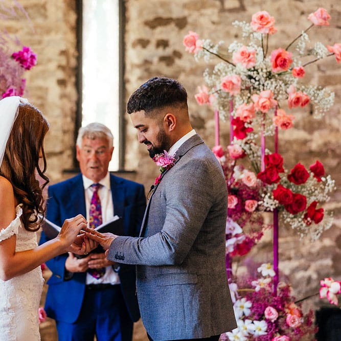 Bride & groom stand in front of bright pink floral wedding arch at the Priston Mill during wedding ceremony 