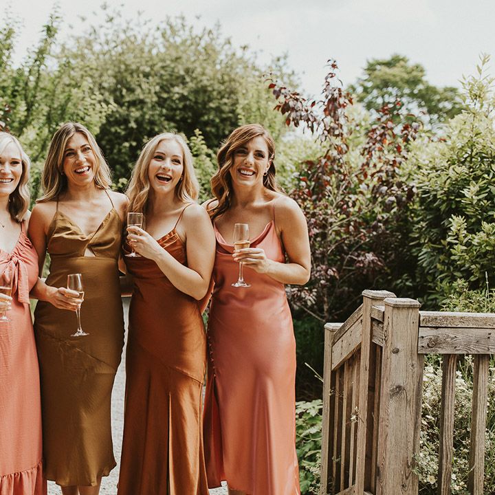 Bridesmaids in mismatched olive, rust and orange coloured dresses 