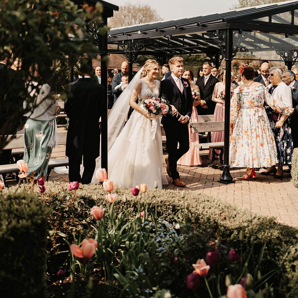 Bride in a lace wedding dress is escorted down the aisle for her outdoor wedding ceremony 