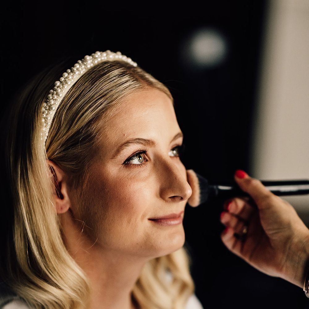 Bride with blonde hair and a pearl headband gets her makeup done for her wedding day 