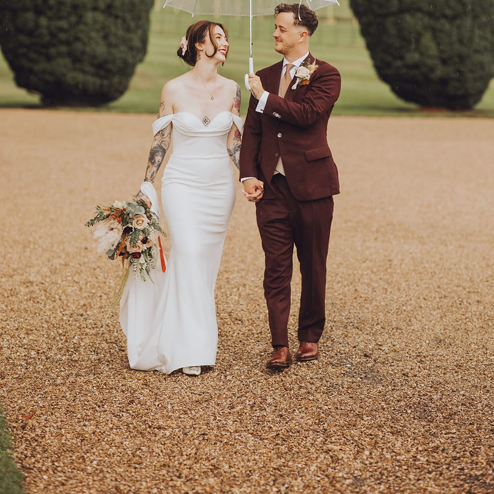 Groom holds clear umbrella above his bride wearing Vera Wang wedding dress and holding Autumnal bouquet 