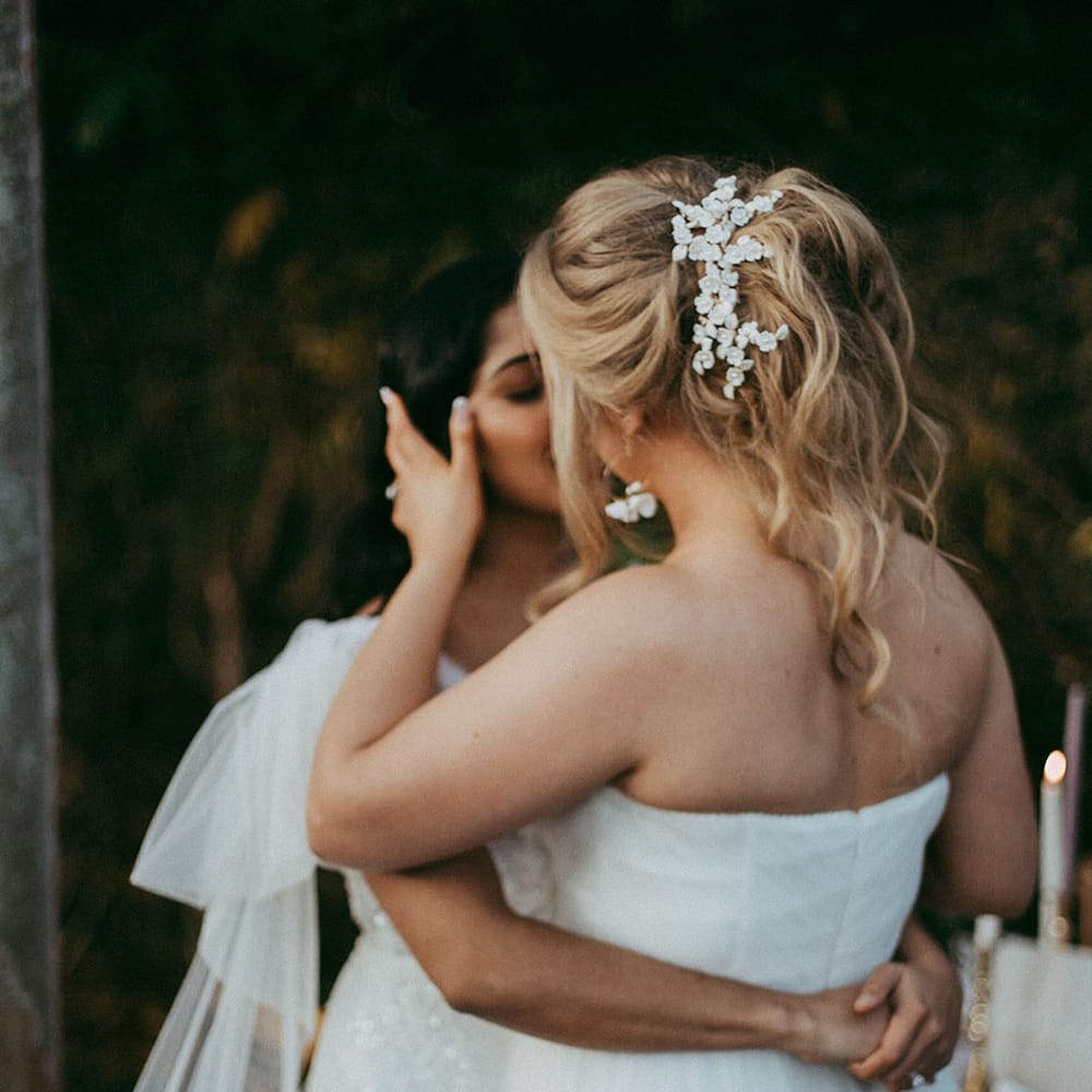 Bride in sleeveless tulle layered wedding dress and bride in short puff sleeve lace wedding dress kissing at the alter of Holesfoot