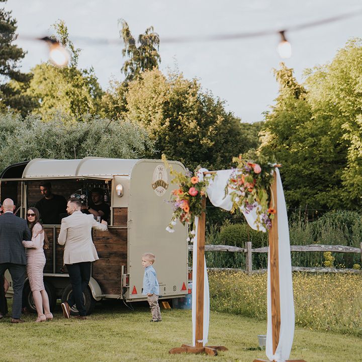 Outdoor truck bar beside wooden arch complete with white drapes and floral decor