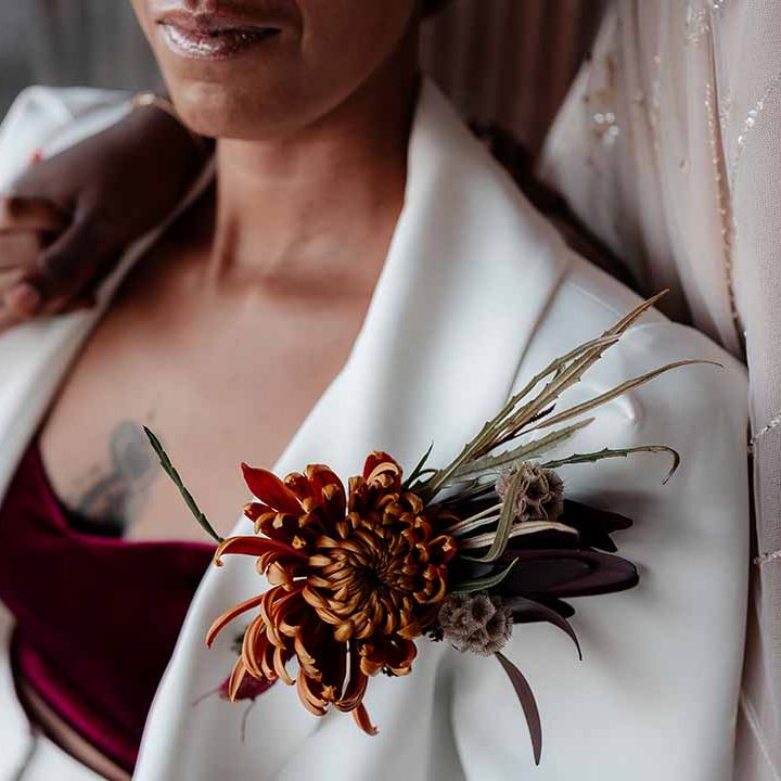 Bride in silk white bridal suit with burgundy v neck crop top and autumnal dried floral boutonniere 