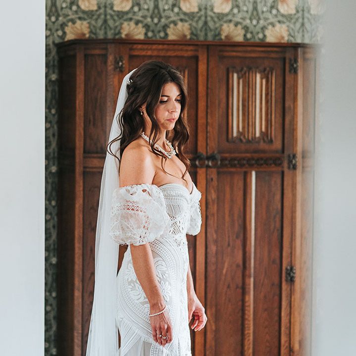 Bride in boho fitted lace wedding dress with detachable sleeves with curled brown hair in a half up half down hairstyle 