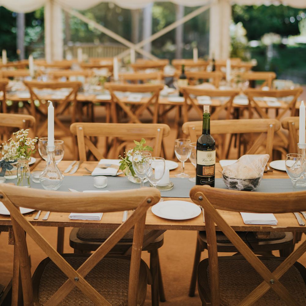 Long wooden wedding tables with blue table runners and bud vases full of daisies in marquee reception at Badgers Holt 