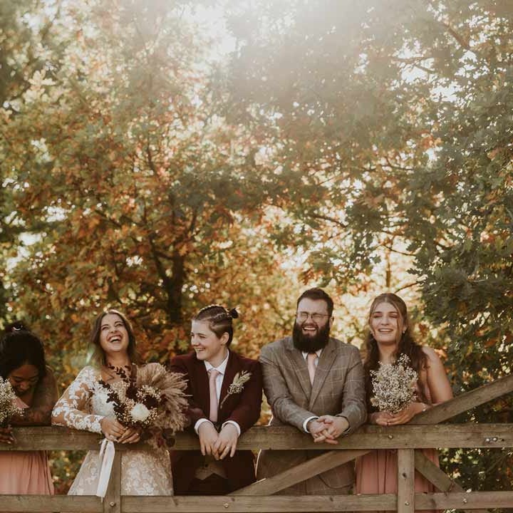 Wedding party with dried flower autumnal bridal bouquets standing on a wooden fence at Bassmead Manor Barns wedding venue 