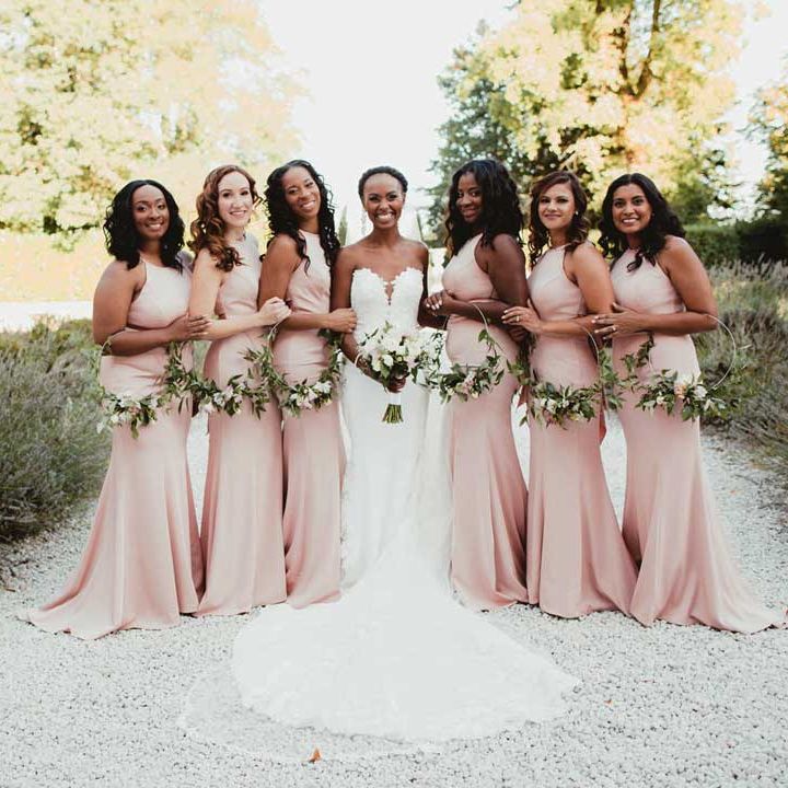 Bride in sleeveless structured wedding dress with puddle train standing with bridesmaids in halterneck pink bridesmaid dresses 