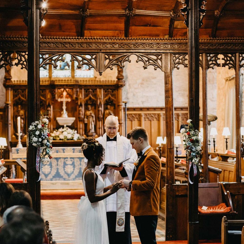 Groom wearing crushed burnt orange velvet grooms blazer standing with bride in v neck sleeveless wedding dress with 3D floral applique train at Brinsop Court wedding