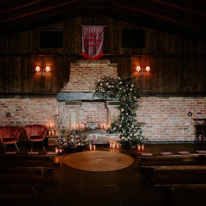 Reception room of Willow Marsh Farm Loughborough with tapered candles, fabric wedding banners, red velvet chairs and large exposed brick fireplace 