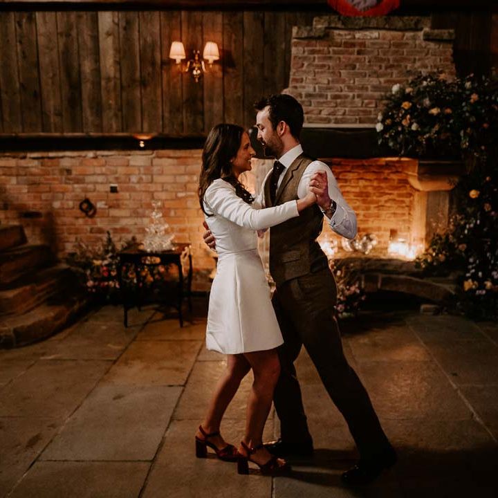 Bride in long sleeve short wedding dress and red velvet chunky wedding heels doing choreographed wedding first dance with groom in brown waistcoat and suit trousers 