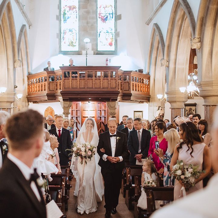 Traditional church wedding ceremony with the bride being walked by the father of the groom down the aisle 