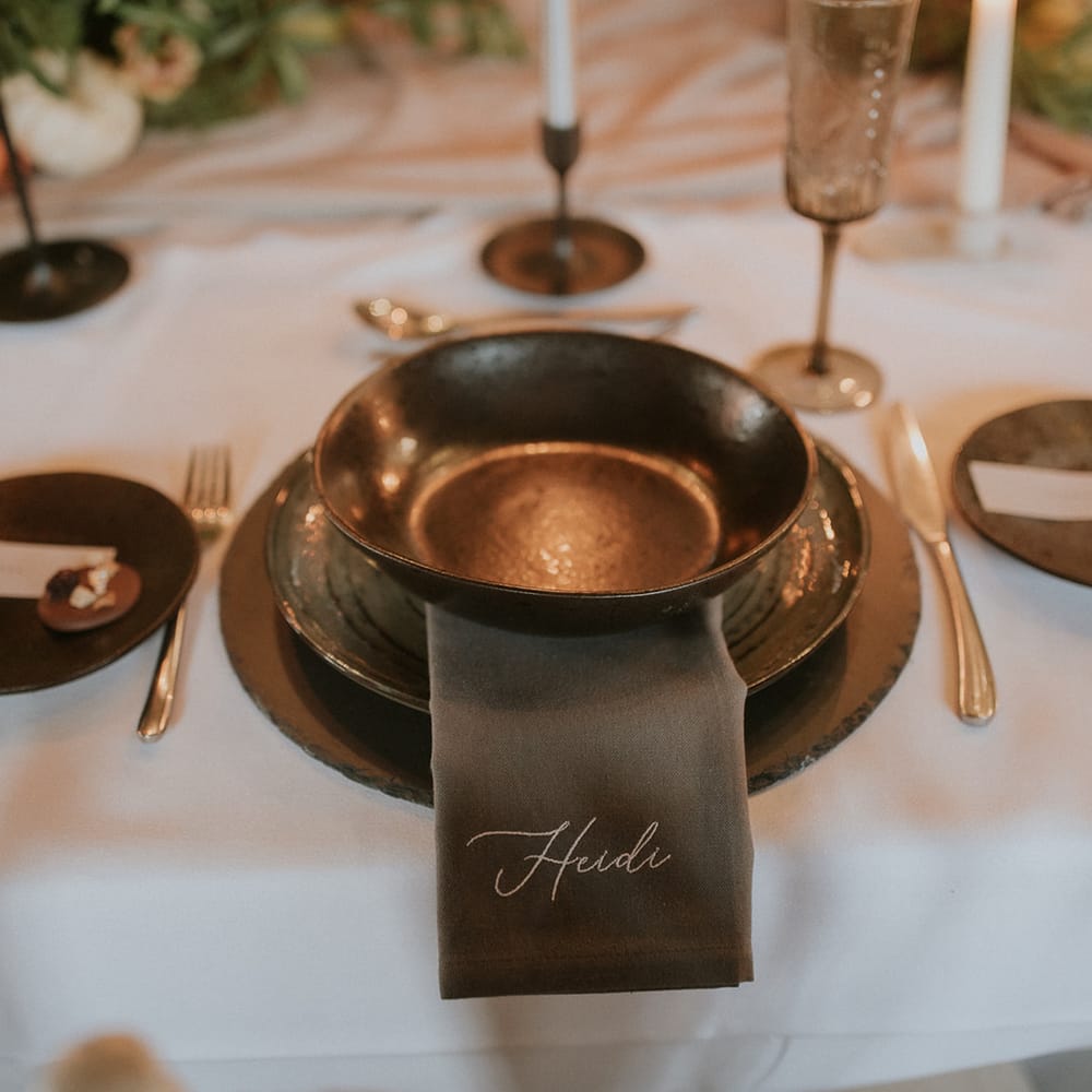 Place setting with coloured table ware and personalised embroidered napkins 