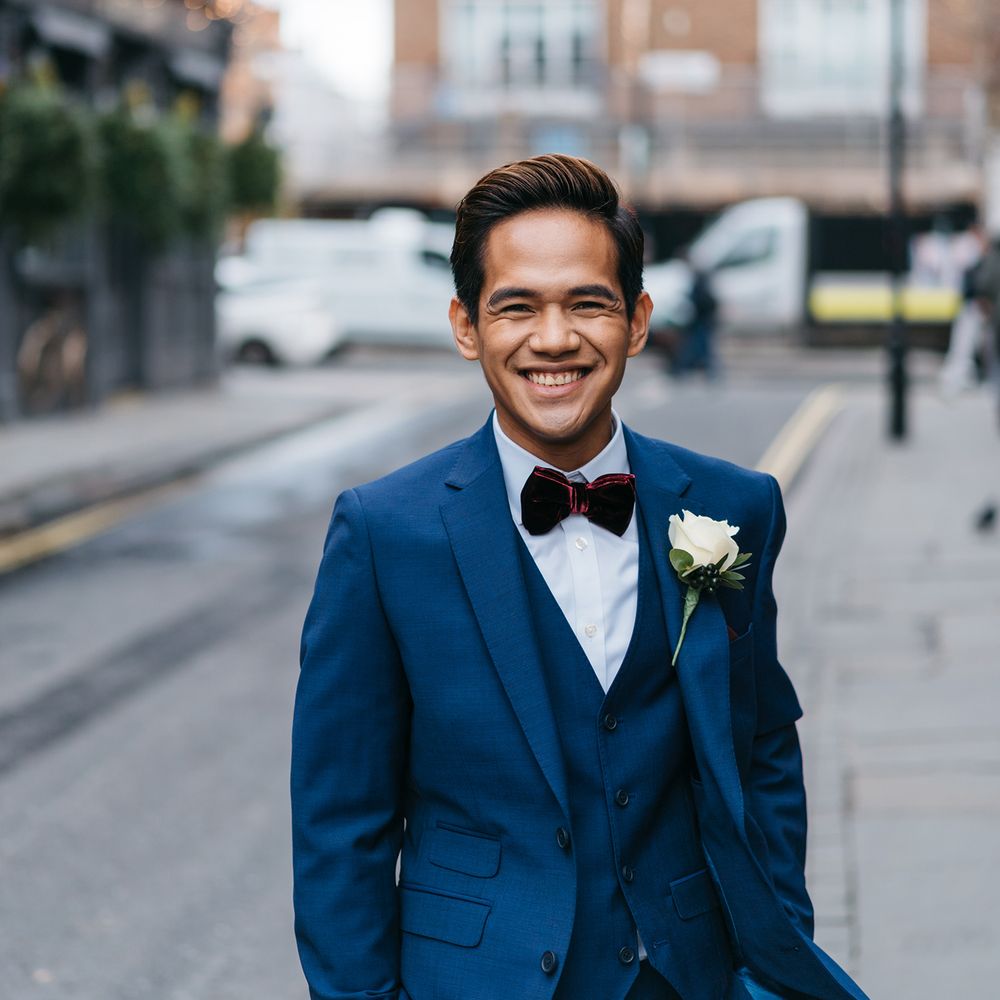 Groom wears blue suit with maroon velvet bow tie