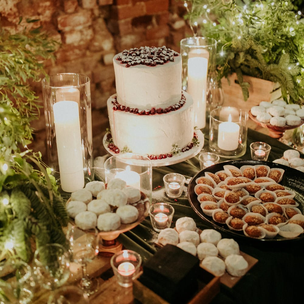 Two tier white wedding cake with red fruit topping, surrounded by traditional festive Greek treats