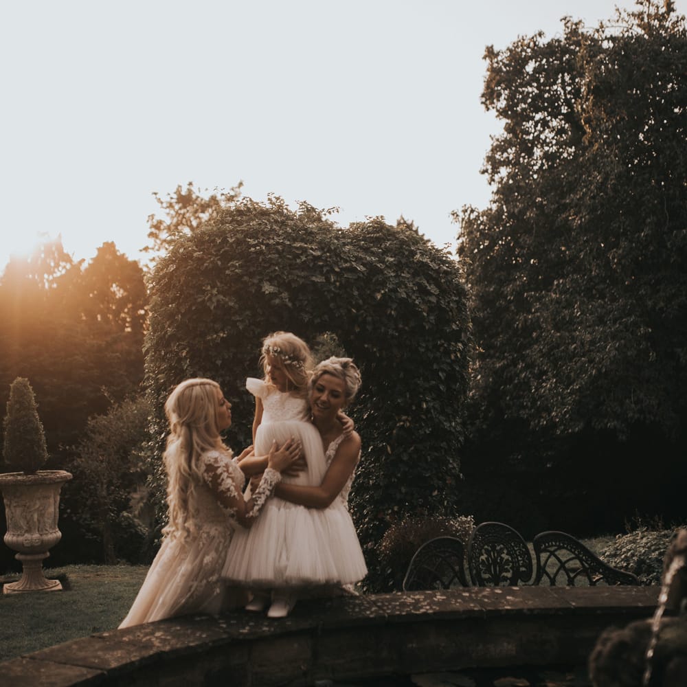 Two brides cuddle their daughter at sunset around a fountain at Crab & Lobster Fairytale Wedding.