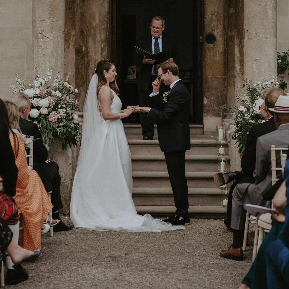 Bride & groom stand in front of staircase leading to large door at Elmore Court on the day of their wedding