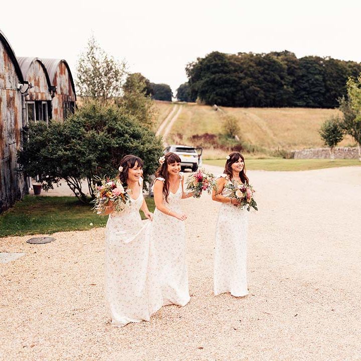 Bridesmaids wear floral bridesmaids dresses and hold colourful bouquets complete with green foliage and bright flowers
