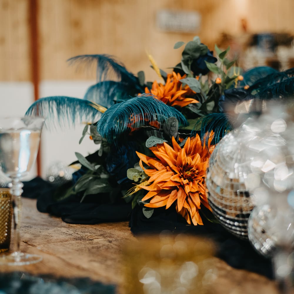 Orange, blue and green floral centrepiece with disco balls and rustic tableware for Wellbeing Farm wedding in Lancashire