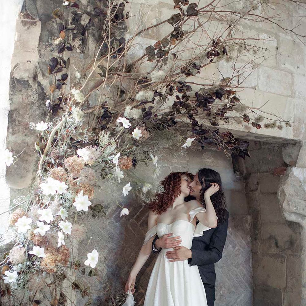 modern gothic wedding inspiration at Blackfriars Priory with bride in a strapless wedding dress kissing her groom in a black suit in a giant fireplace 