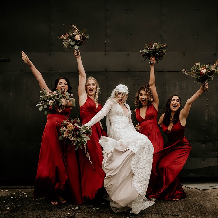 Bridal party portrait with bride in a lace wedding dress and bridesmaids in red satin bridesmaid dresses 