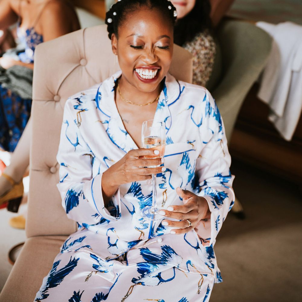 Black bride on the wedding morning in patterned satin pyjamas drinking champagne 