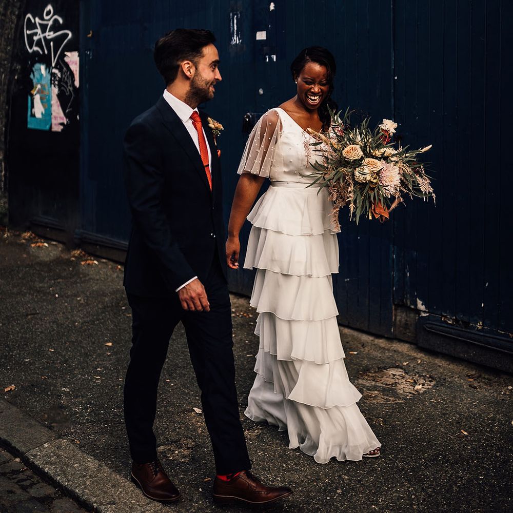 Urban bride and groom portrait in London with Black bride in a layered tulle wedding dress and groom in a navy blue suit 