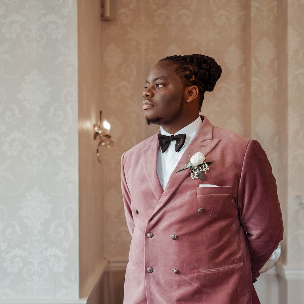 Groom wears dusky pink suit on his wedding day complete with floral buttonhole 