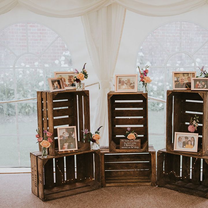 Area of wooden crates with family photos of late family members with fairy lights, decorative wooden plaque and flowers