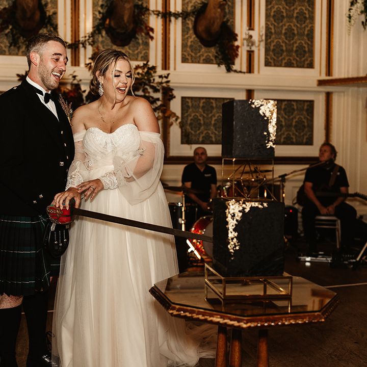 Bride and groom cut their two tier black wedding cake with gold flakes with a sword 