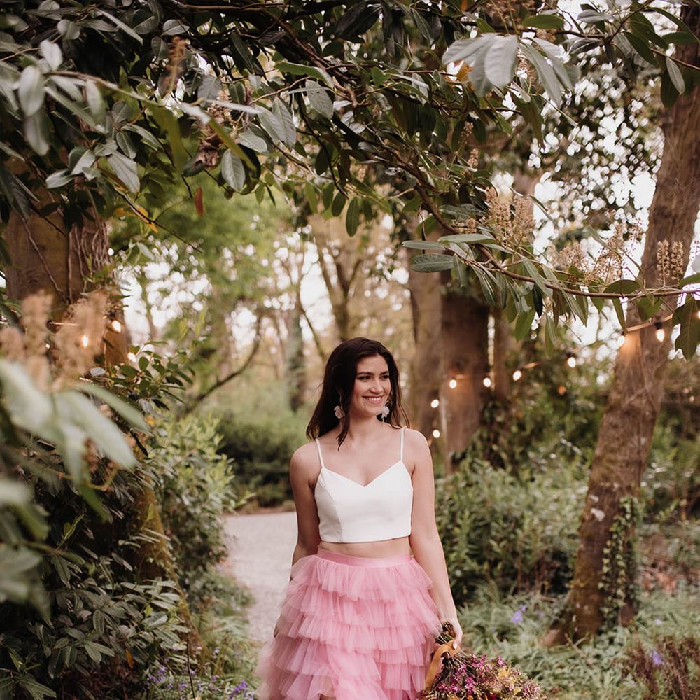 Bride in a white crop top and layered pink tulle skirt with front slit holding a pink and yellow wildflower wedding bouquet 