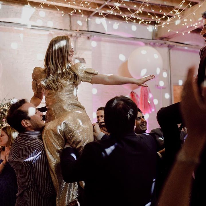 Bride and groom are lifted up on chairs for wedding reception with fairy lights and white balloon decoration 