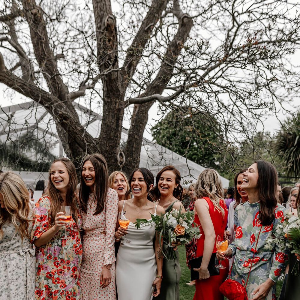 Bride in a white satin wedding dress laughing with her friends at her back garden wedding 