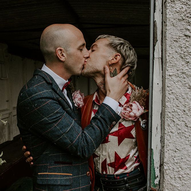 Groom wears colourful shirt and orange velvet blazer as he kisses his groom outdoors 