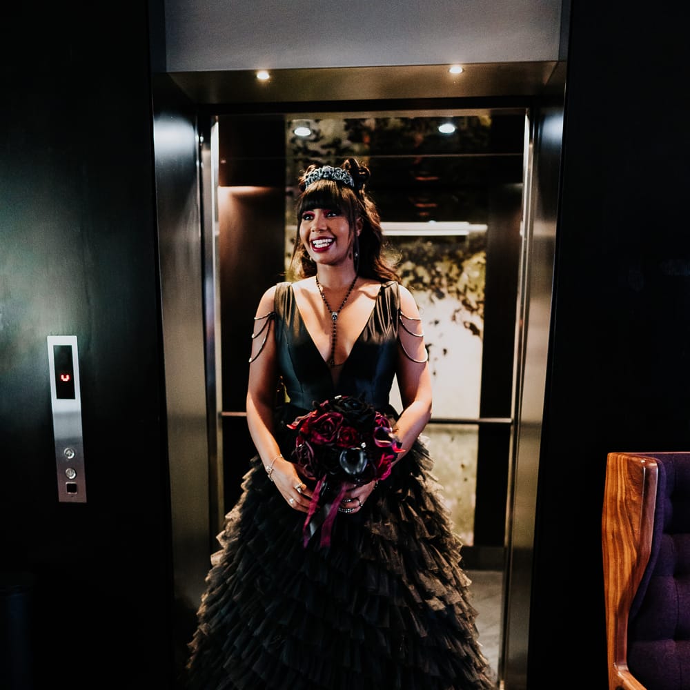 Bride wears black ruffled wedding dress complete with shoulder detailing and skull crown for gothic look 
