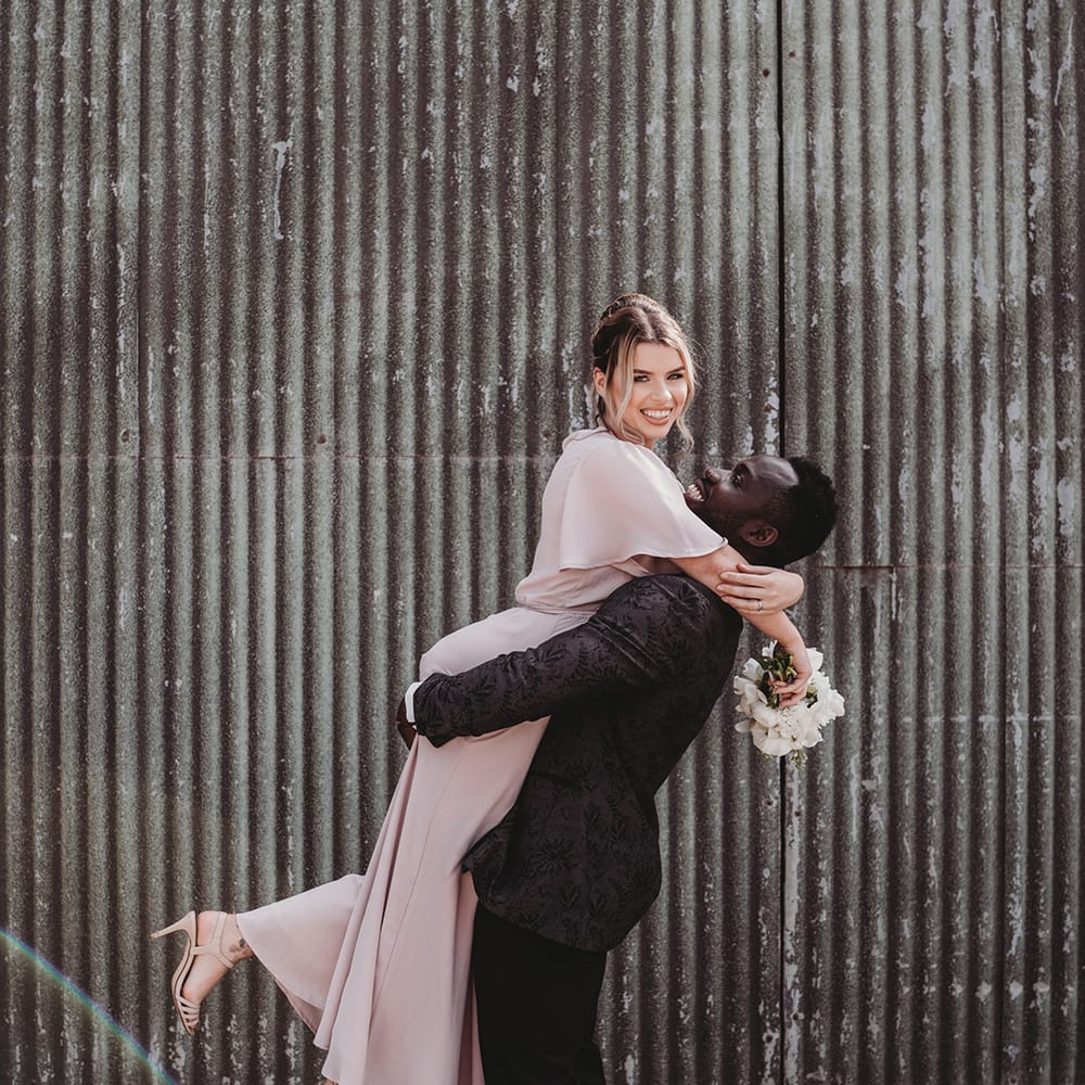 Groomsmen in a patterned suit jacket lifting up a bridesmaid in a pale pink dress