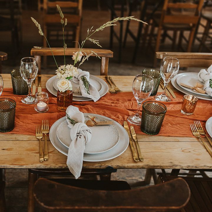 Orange table runner with gold cutlery, coloured glassware and plain plates for the table settings 